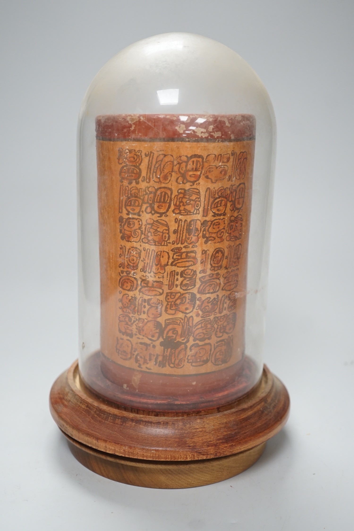 A Mayan pigment painted terracotta cylindrical vessel, possibly 7th-9th century AD., 17.2cm high, under a glass dome with revolving wood stand, total height 26cm
